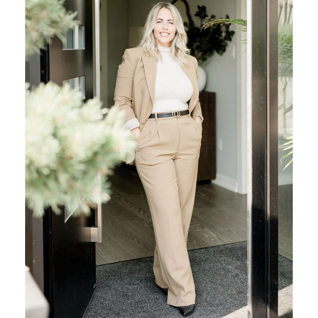 Woman with blond hair standing between floor to ceiling front door with different types of plants around her.