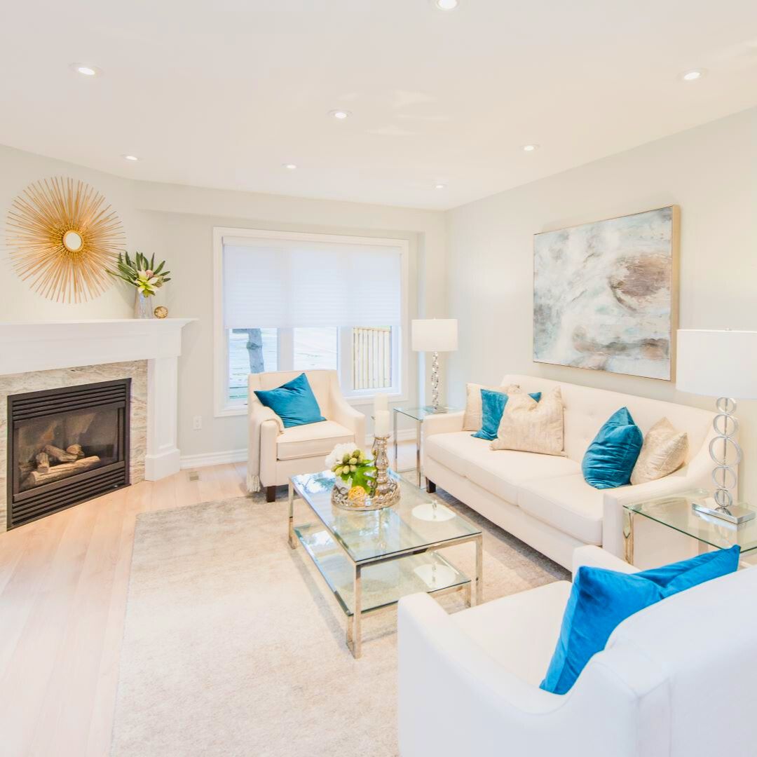 Elegant open-concept living space: luxurious dining area with glass-top table, plush upholstered chairs, and statement pendant light. Seamless flow to cozy living room featuring fireplace and coastal accents
