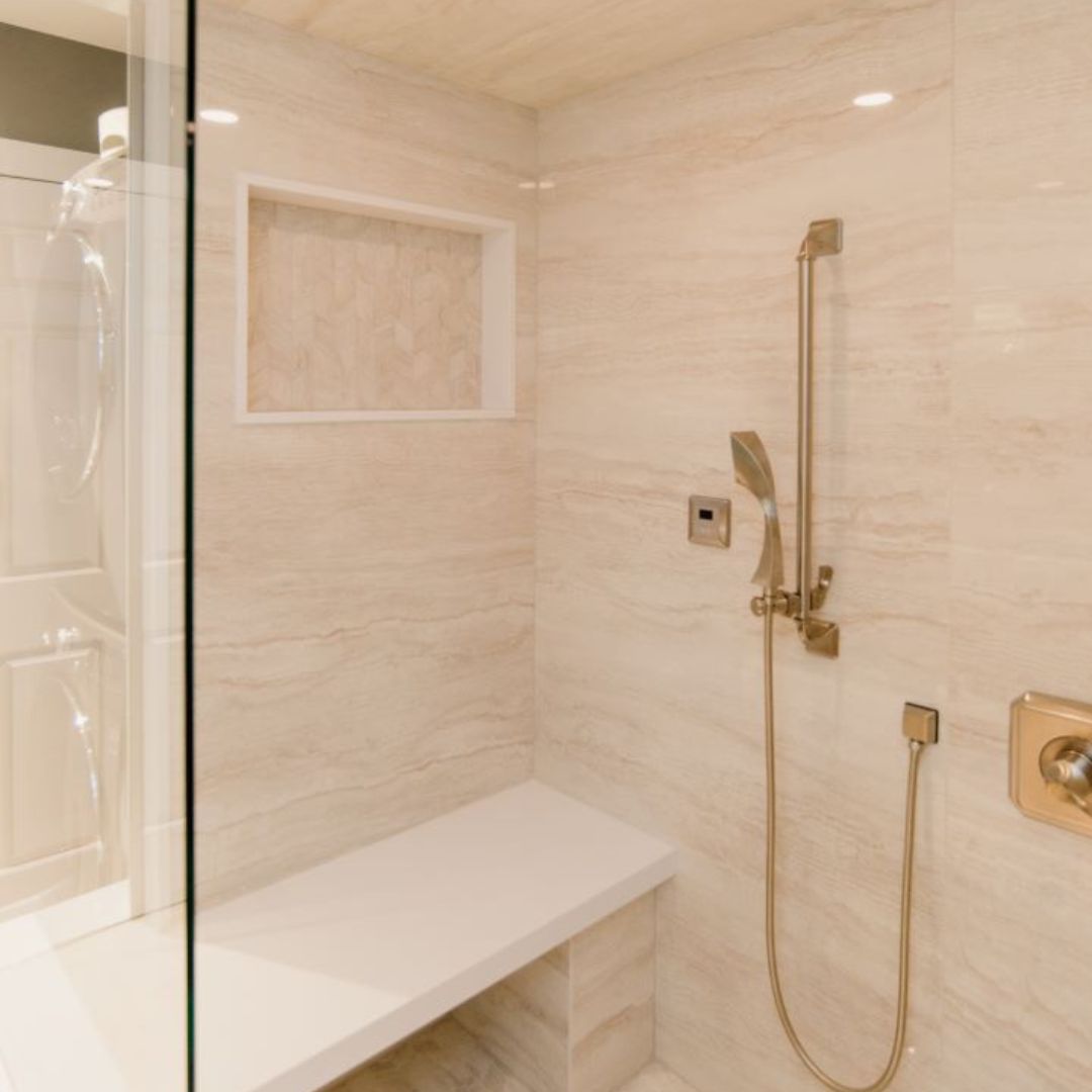 Luxurious walk-in shower with beige tile walls, built-in shelf, and gold-toned shower fixtures, showcasing modern bathroom design