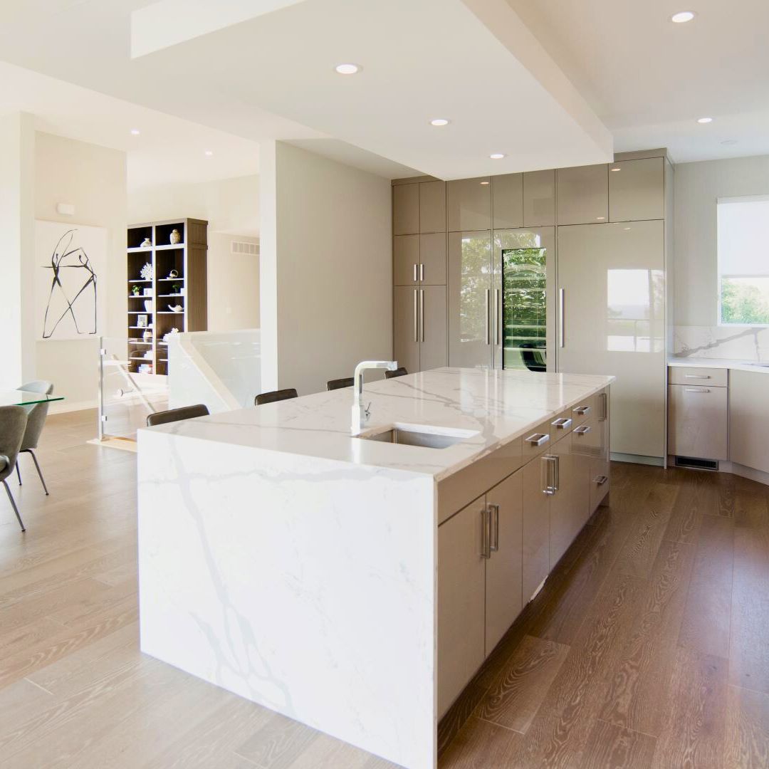 Modern penthouse kitchen design in Hamilton, Ontario featuring a large marble waterfall island, sleek high-gloss cabinetry, and integrated appliances. Includes open-concept layout with contemporary finishes and a minimalist aesthetic.