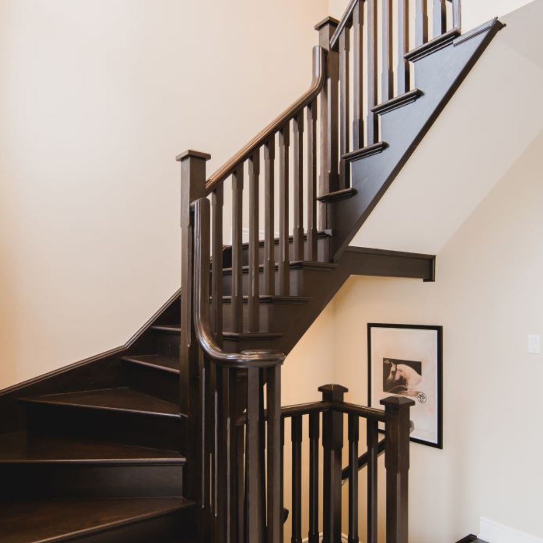 Elegant custom staircase with dark wood finish and curved handrail. White walls contrast beautifully with the rich wood tones. Framed artwork adds a personal touch to the stairway.