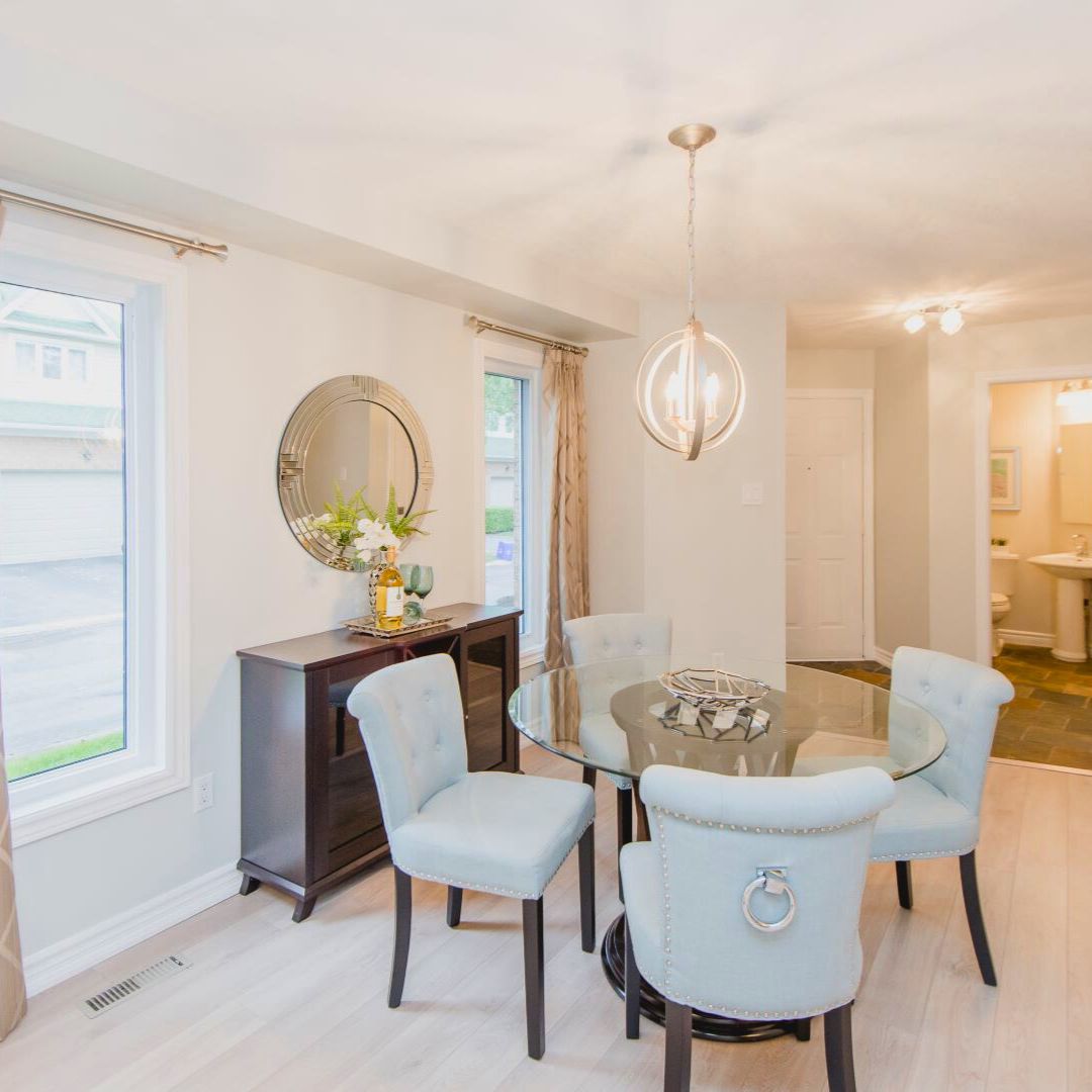 Stylish dining room with glass table, light blue chairs, modern chandelier, and decorative circular mirror