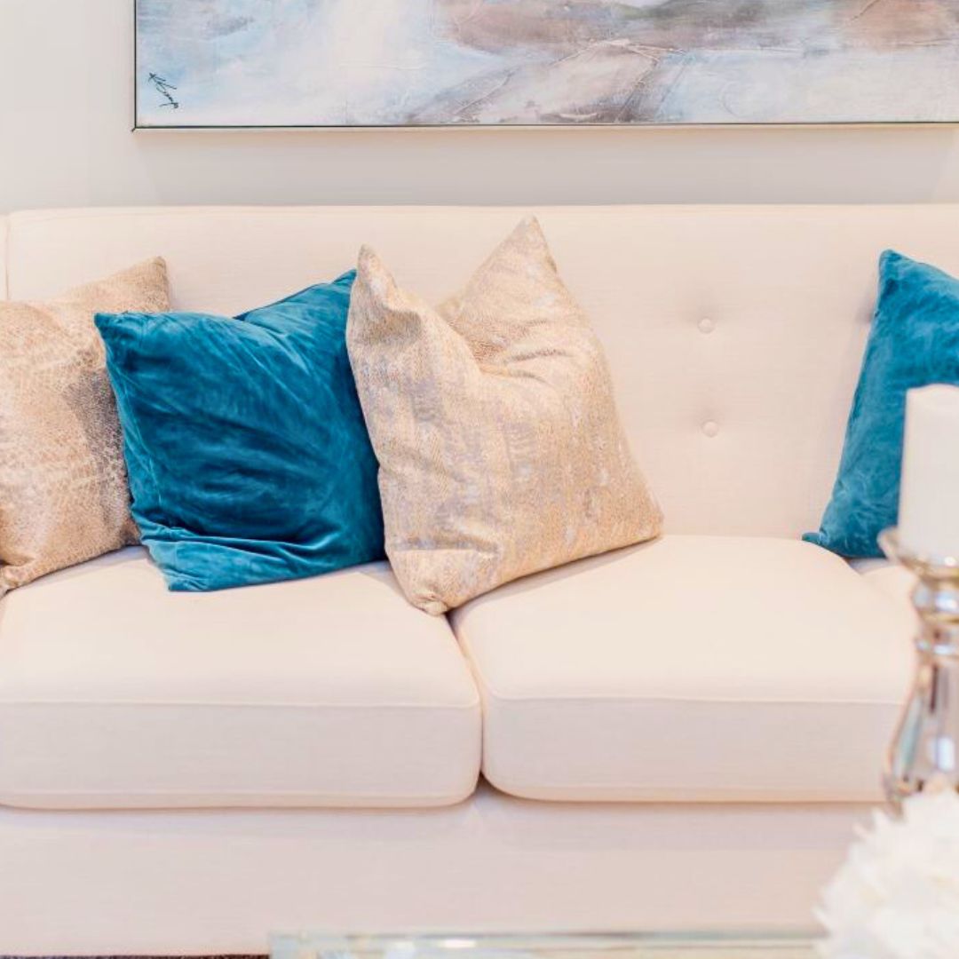 Elegant living room design with cream sofa, teal blue and gold accent pillows, and abstract wall art