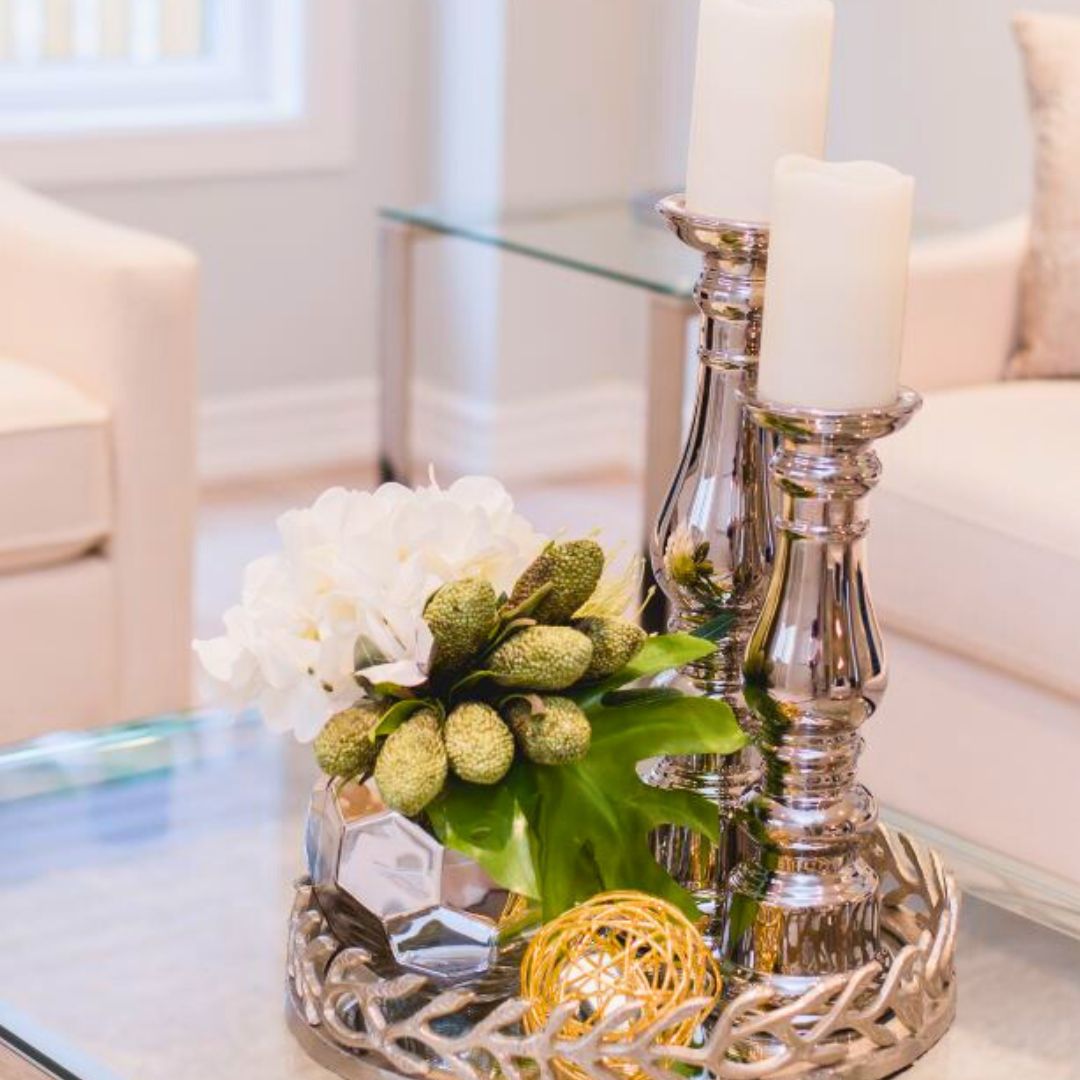 Elegant coffee table decor with white flowers, silver candlesticks, and decorative objects on a glass surface