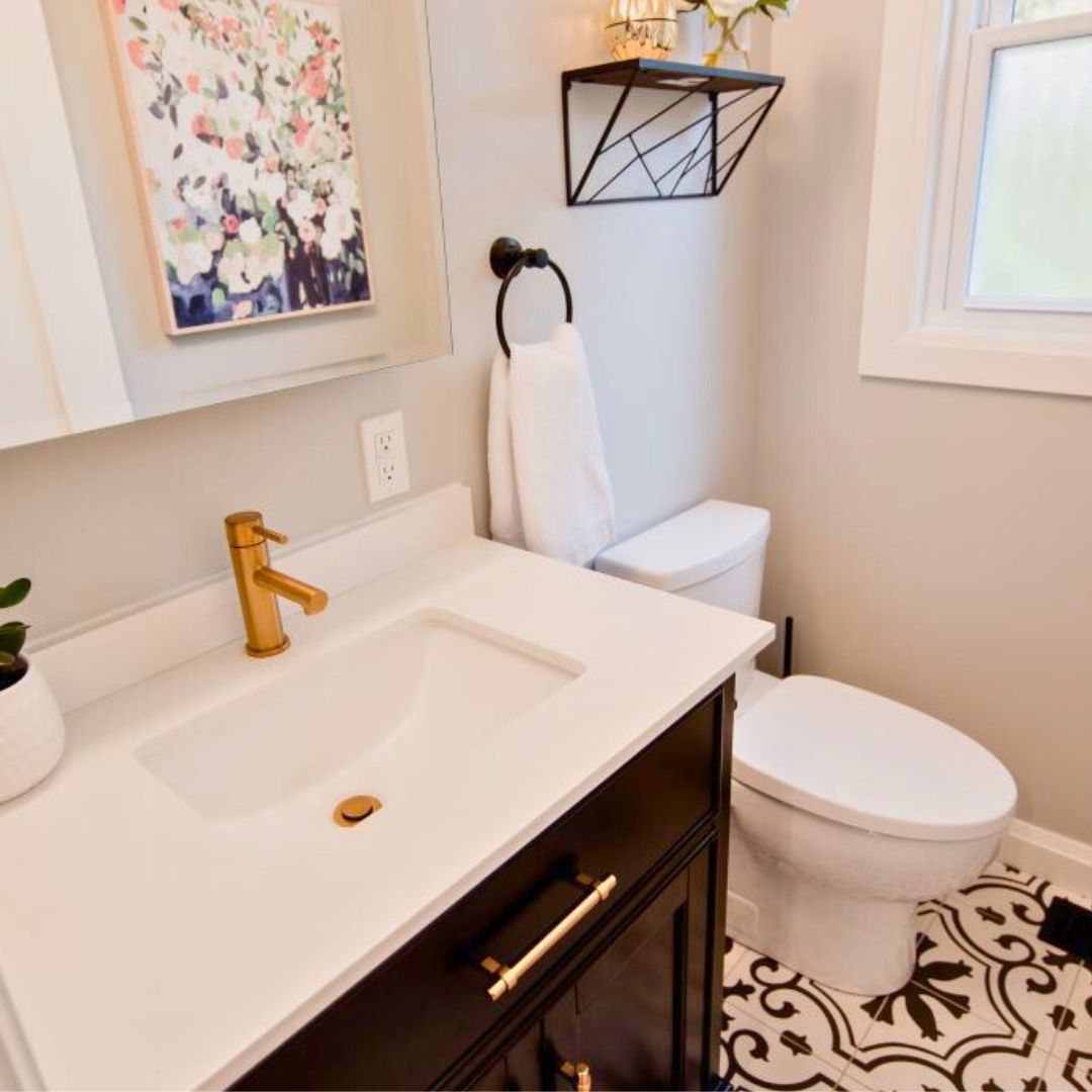 Bright bathroom with white vanity, gold faucet and shelf, floral artwork, and patterned floor tiles