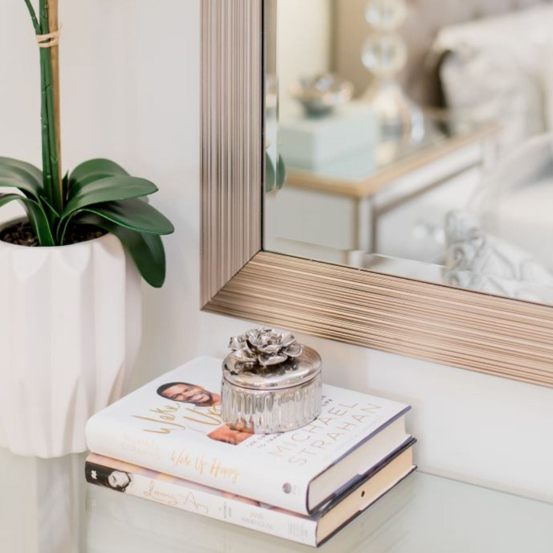 Bedroom vanity with gold-framed mirror, potted orchid, decorative books, and silver accents, reflecting chic interior design touches