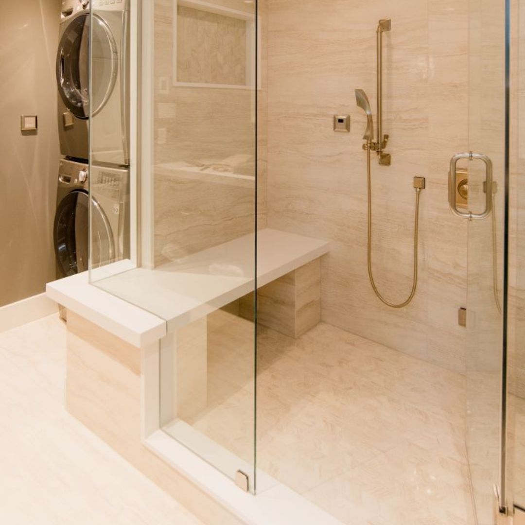 Elegant walk-in shower featuring floor-to-ceiling beige marble tiles, gold-finish shower fixtures, a built-in marble bench, recessed lighting, and a frameless glass door, exemplifying high-end bathroom design and luxury home renovations.
