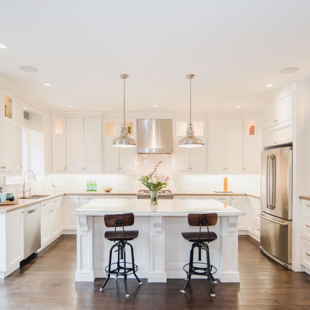 Bright, modern kitchen with white cabinetry, stainless steel appliances, and large center island. Industrial-style pendant lights hang above island with stylish bar stools. Open floor plan and recessed lighting create an airy feel.