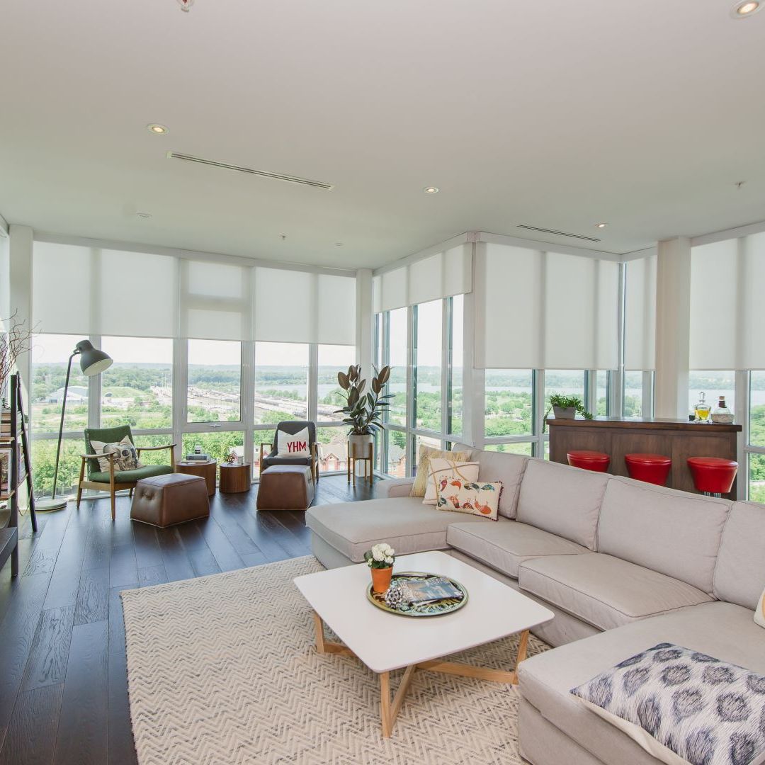 Spacious luxury apartment  living area with floor-to-ceiling windows, light-colored furniture, and a stylish rug, showcasing a modern urban lifestyle.