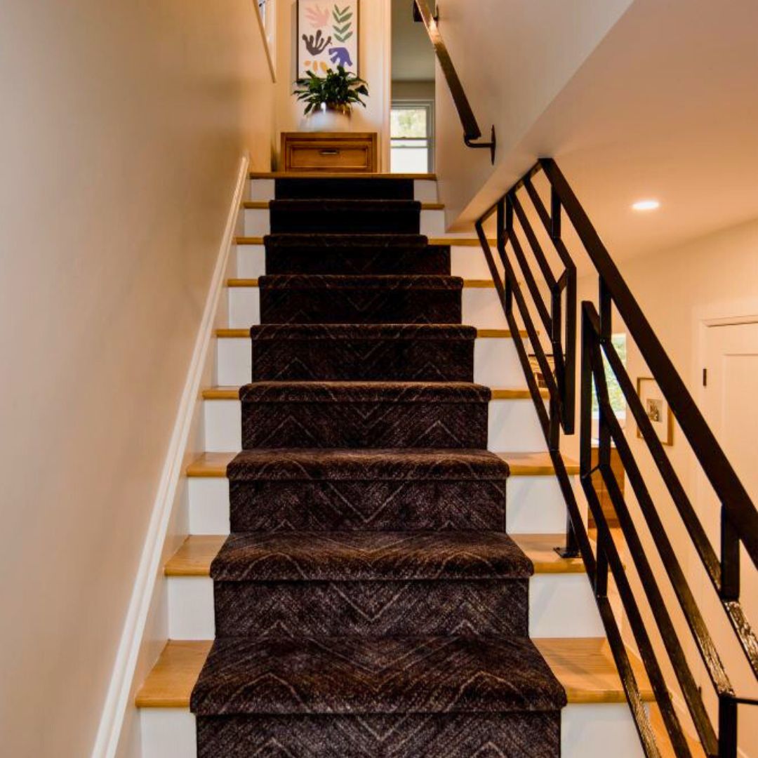 Elegant staircase with dark carpet runner, wooden steps, and black metal railing leading upstairs