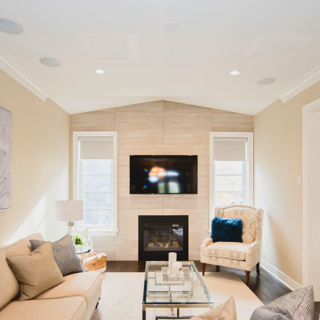 Cozy living room with beige walls, fireplace, and wall-mounted TV. Comfortable seating and glass coffee table create an inviting space