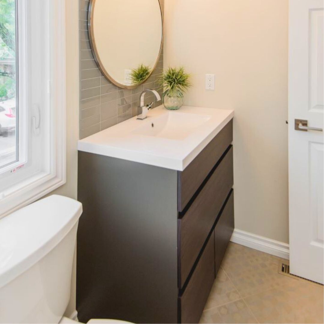 Modern bathroom featuring a floating dark wood vanity with white countertop. Round mirror and gray tile backsplash create a sleek look.