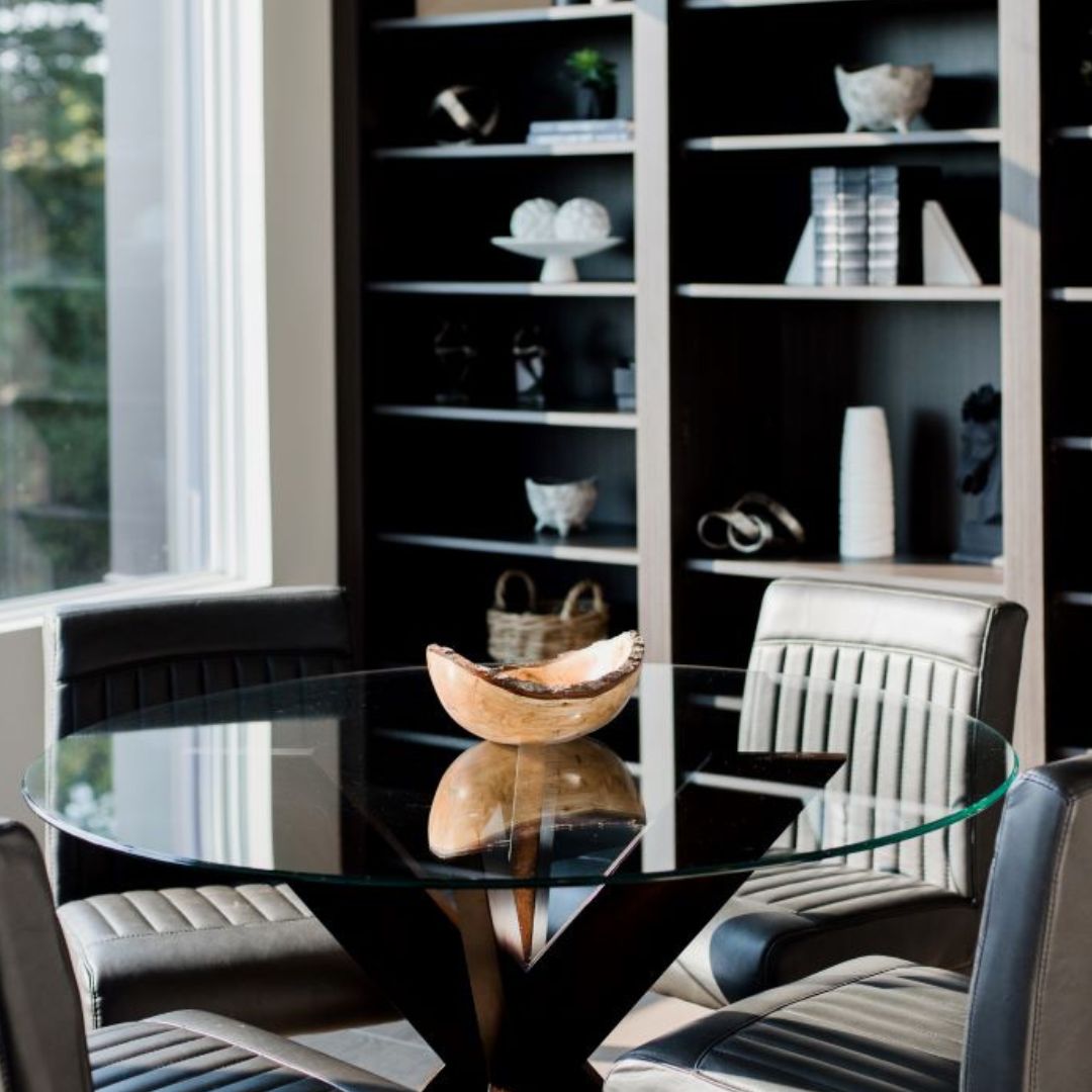 Elegant dining space with glass table and black chairs. Floor-to-ceiling built-in shelving showcases decorative items. White couch in foreground, blending modern and cozy aesthetics.