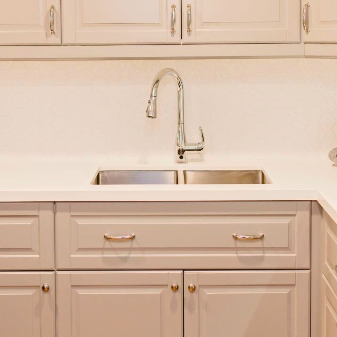 Close-up of undermount double sink with sleek chrome pull-down faucet. White quartz countertop and light beige shaker cabinets visible