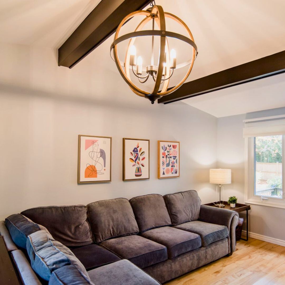 living room featuring plush charcoal sectional sofa, brass orb chandelier with candle lights, abstract wall art triptych, and warm wood flooring