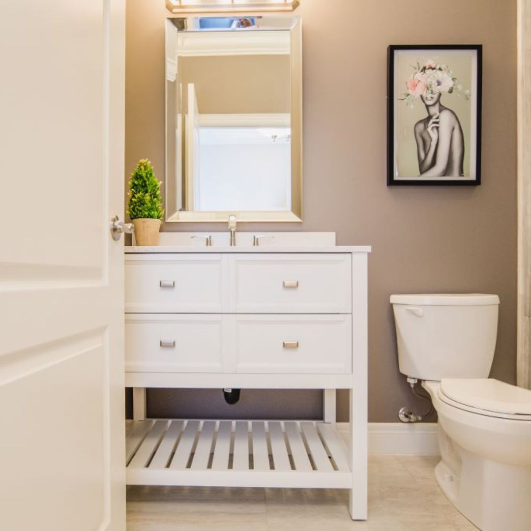 Bright bathroom featuring a white vanity with drawers, framed mirror, modern lighting, and artistic wall decor, creating a stylish and functional space.