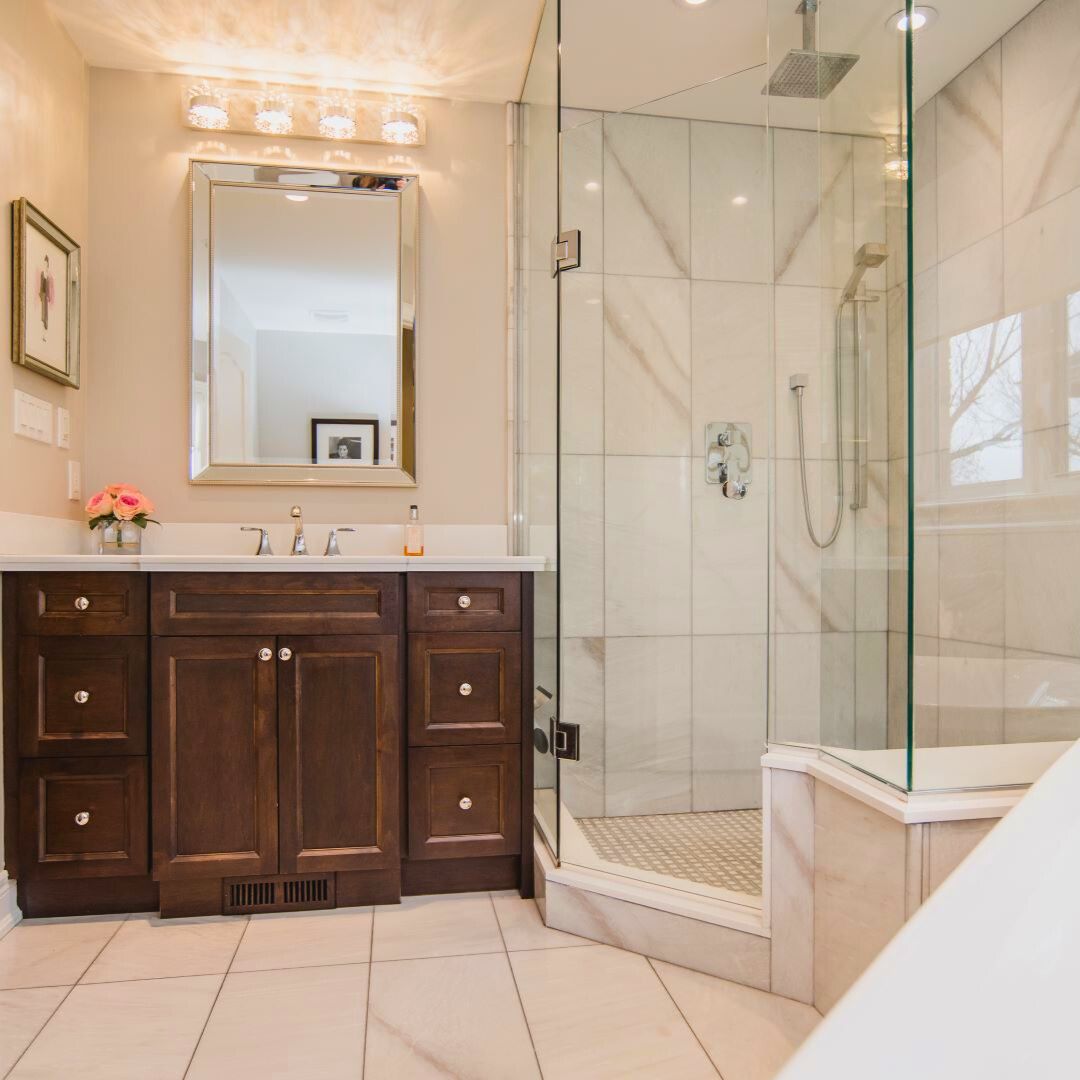 elegant bathroom design with dark wood vanity, white countertop, and framed mirror. Crystal light fixtures and a vase of flowers add elegance to the warm, inviting space.