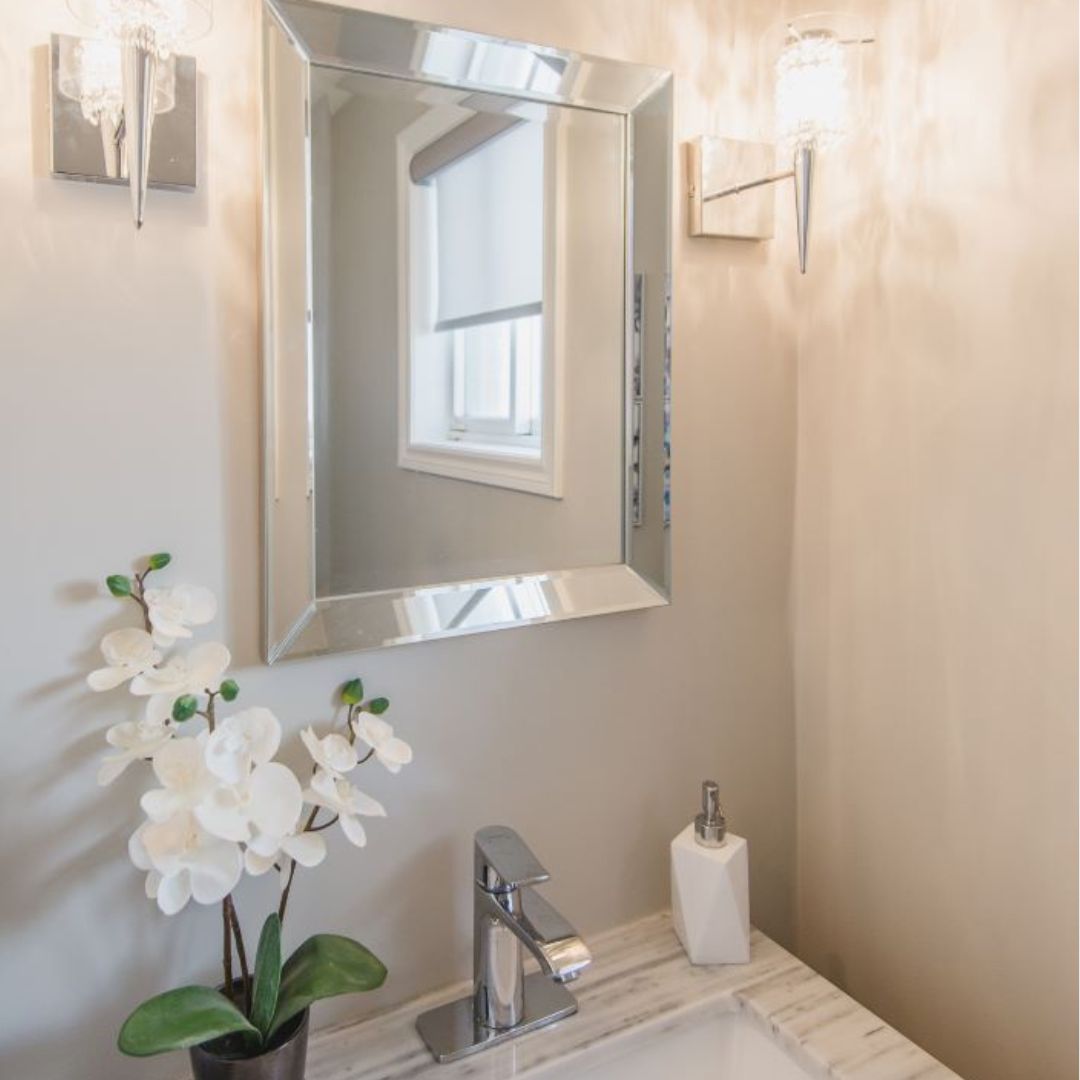 Elegant bathroom vanity with white orchid, framed mirror, and crystal wall sconces creating a luxurious atmosphere.