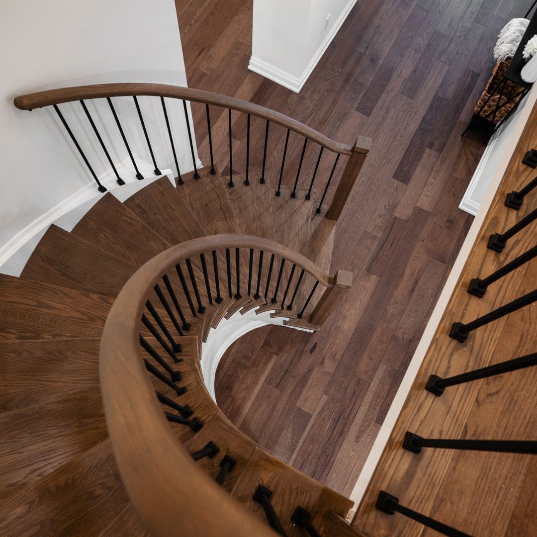 Elegant curved wooden staircase design in Hamilton, Ontario featuring a smooth handrail and black iron balusters.