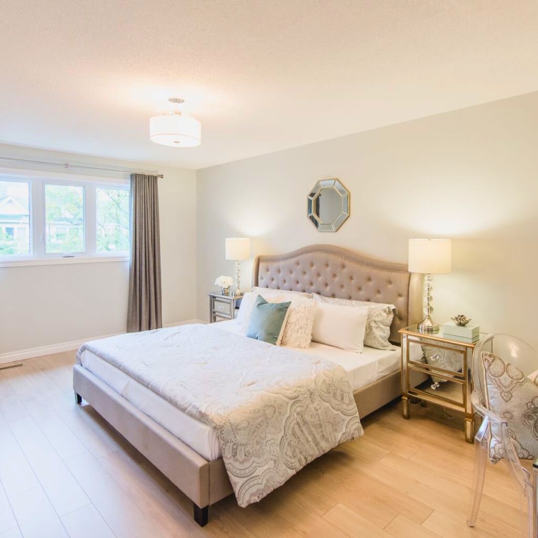 Master bedroom with tufted beige headboard, mirrored nightstands, drum pendant light, and octagonal wall mirror, showcasing elegant neutral color scheme and hardwood floors