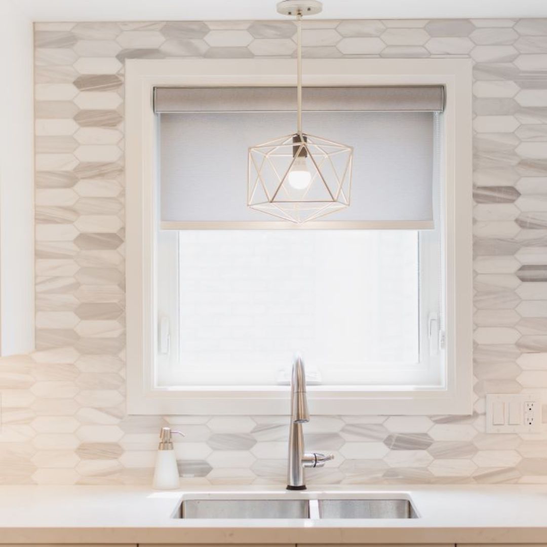 Stylish kitchen sink area with hexagon tile backsplash, white cabinets, and geometric pendant light. Modern faucet and window create a fresh, clean look