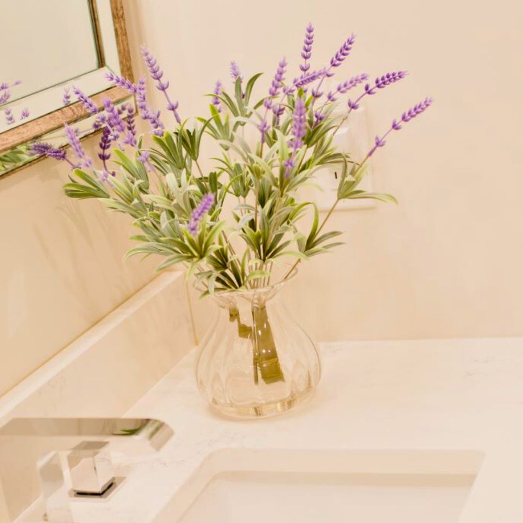 Purple lavender flowers in a clear glass vase on a white countertop, adding a pop of color to a bright bathroom setting.