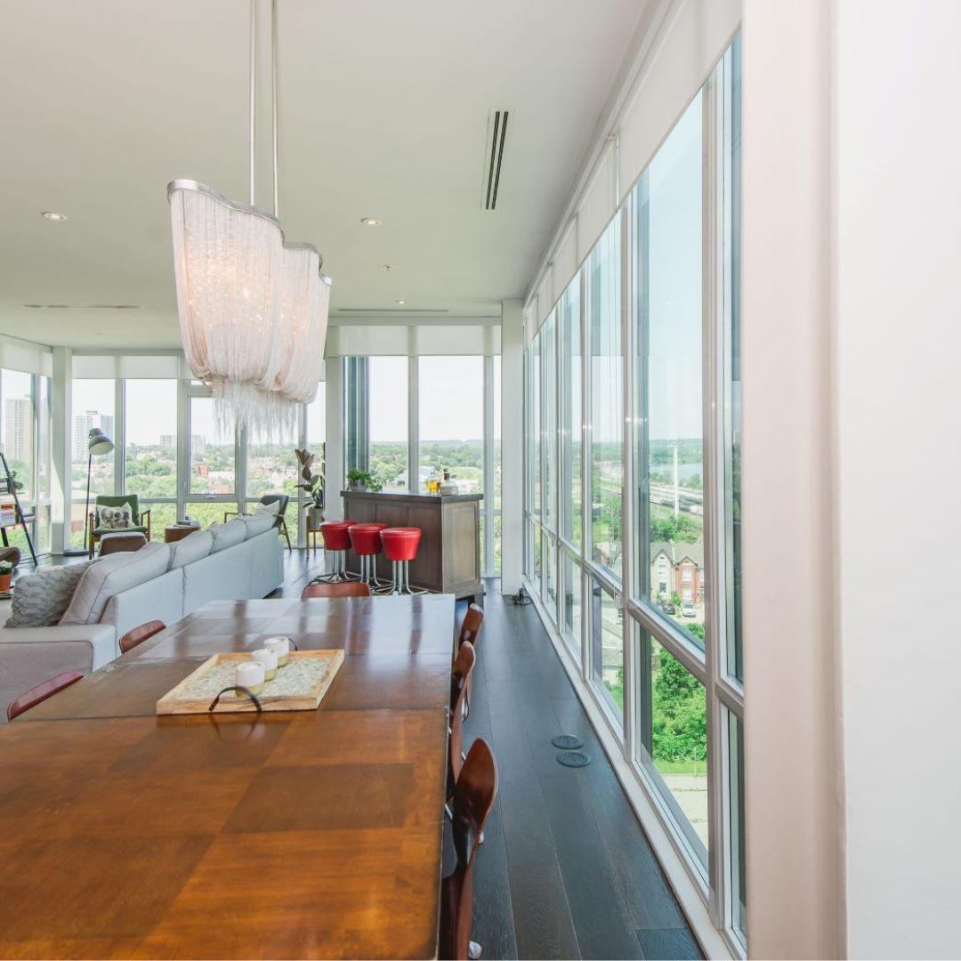 Spacious luxury apartment living room with panoramic windows, featuring a wooden dining table, modern chandelier, and stunning city views