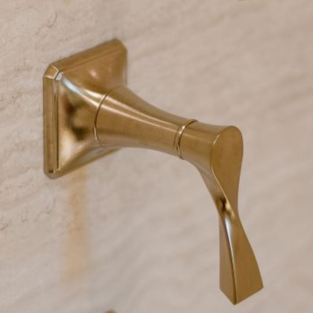 Detailed view of an opulent gold-finish bathroom towel hook with a unique twisted design, mounted on a smooth beige wall. The hook's sculptural form adds an artistic touch to high-end bathroom accessories and luxurious interior details.