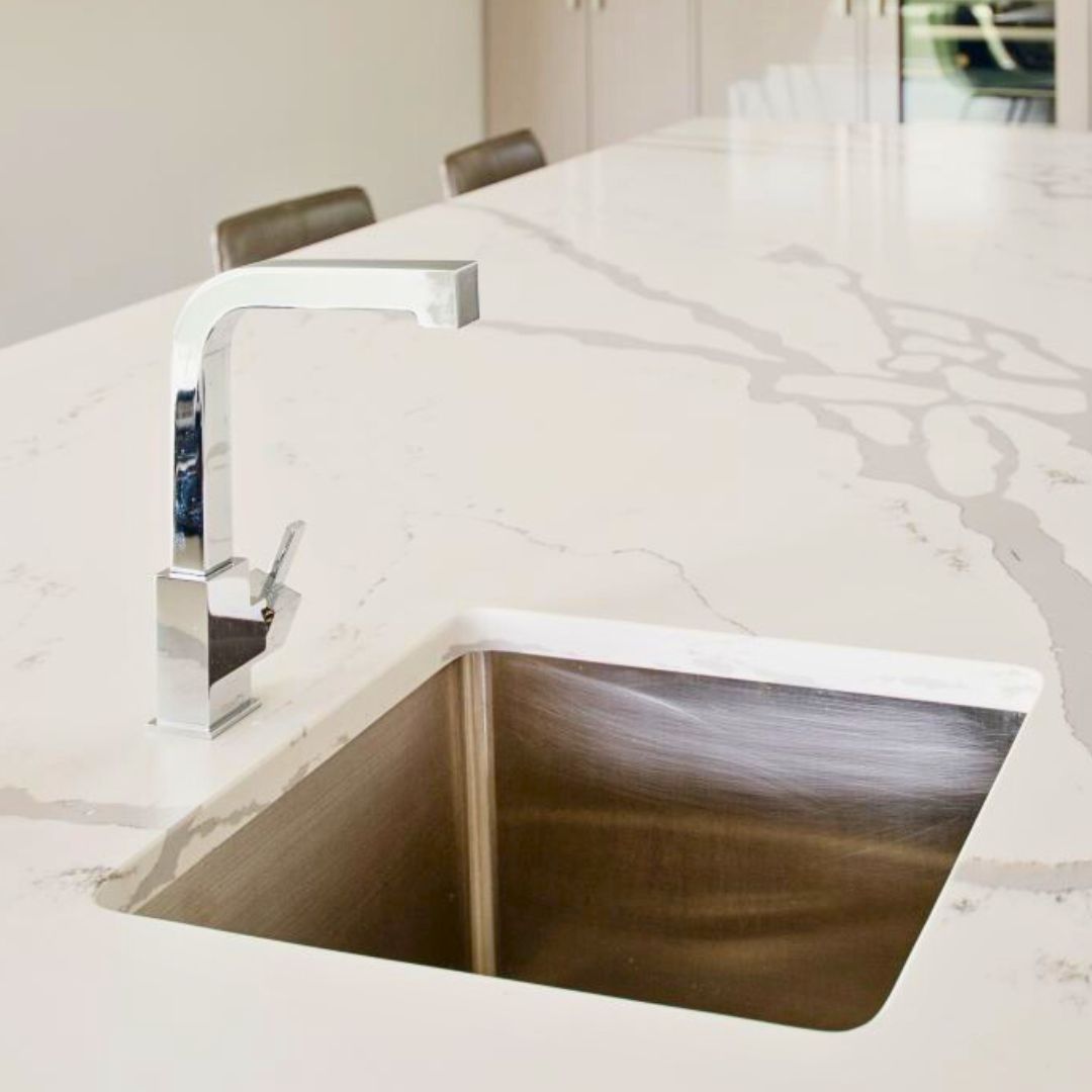 Sleek kitchen island with luxurious white marble countertop, featuring a modern square stainless steel sink and stylish chrome faucet. The countertop's elegant veining adds sophistication to this high-end kitchen design.