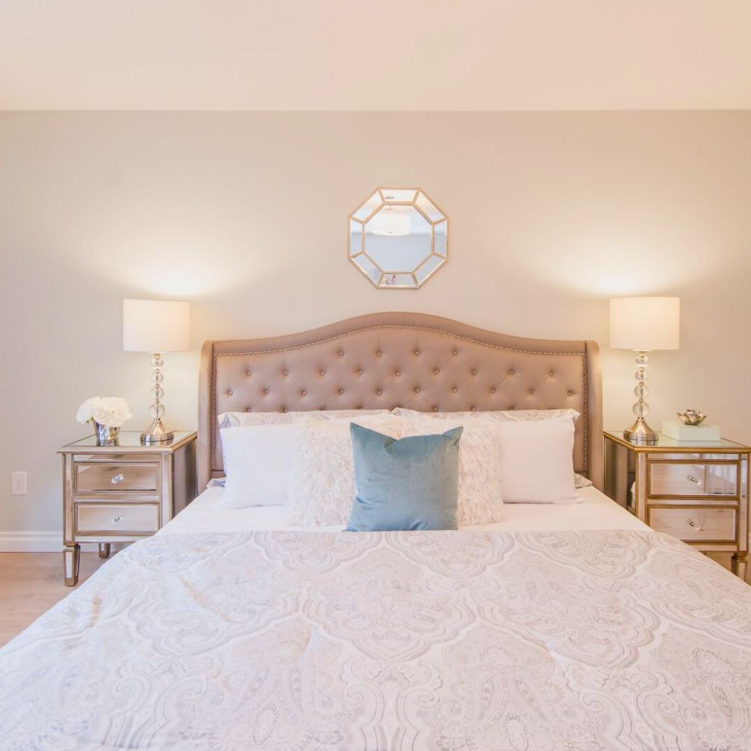 Serene master bedroom with tufted beige headboard, mirrored nightstands, and octagonal wall mirror