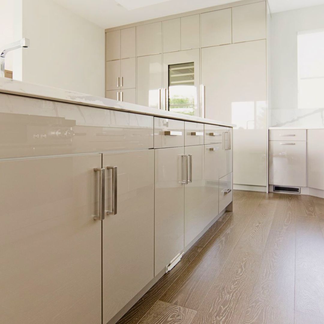 glossy taupe cabinets and white marble waterfall countertop. Light wood floors and stainless steel appliances complete the high-end, modern look.