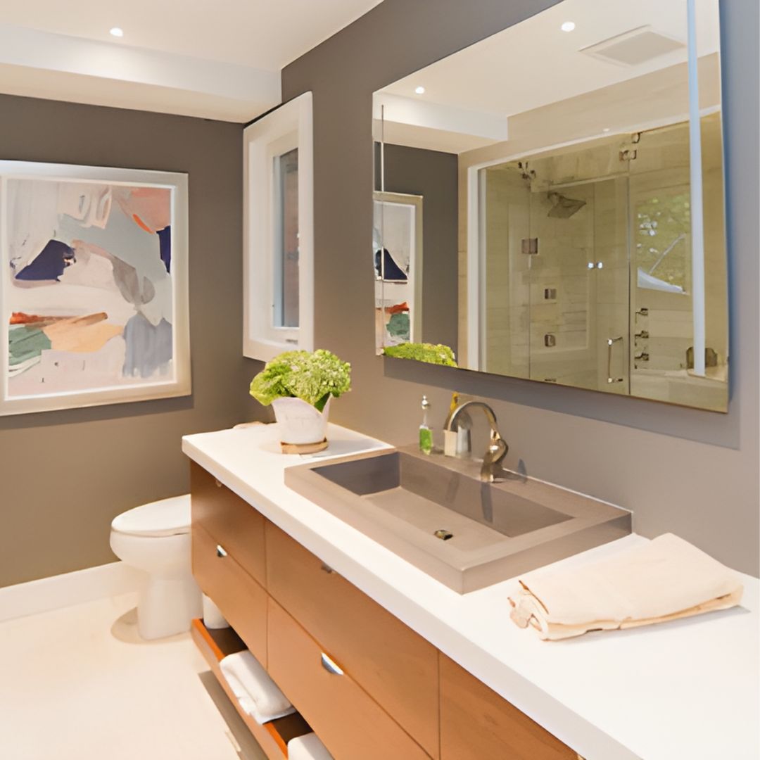 Modern bathroom with custom walnut vanity, white quartz countertop, stylish hardware, and integrated lighting mirror. Chic gray walls, abstract art, and a potted plant create a sophisticated look, perfect for upscale home renovations 