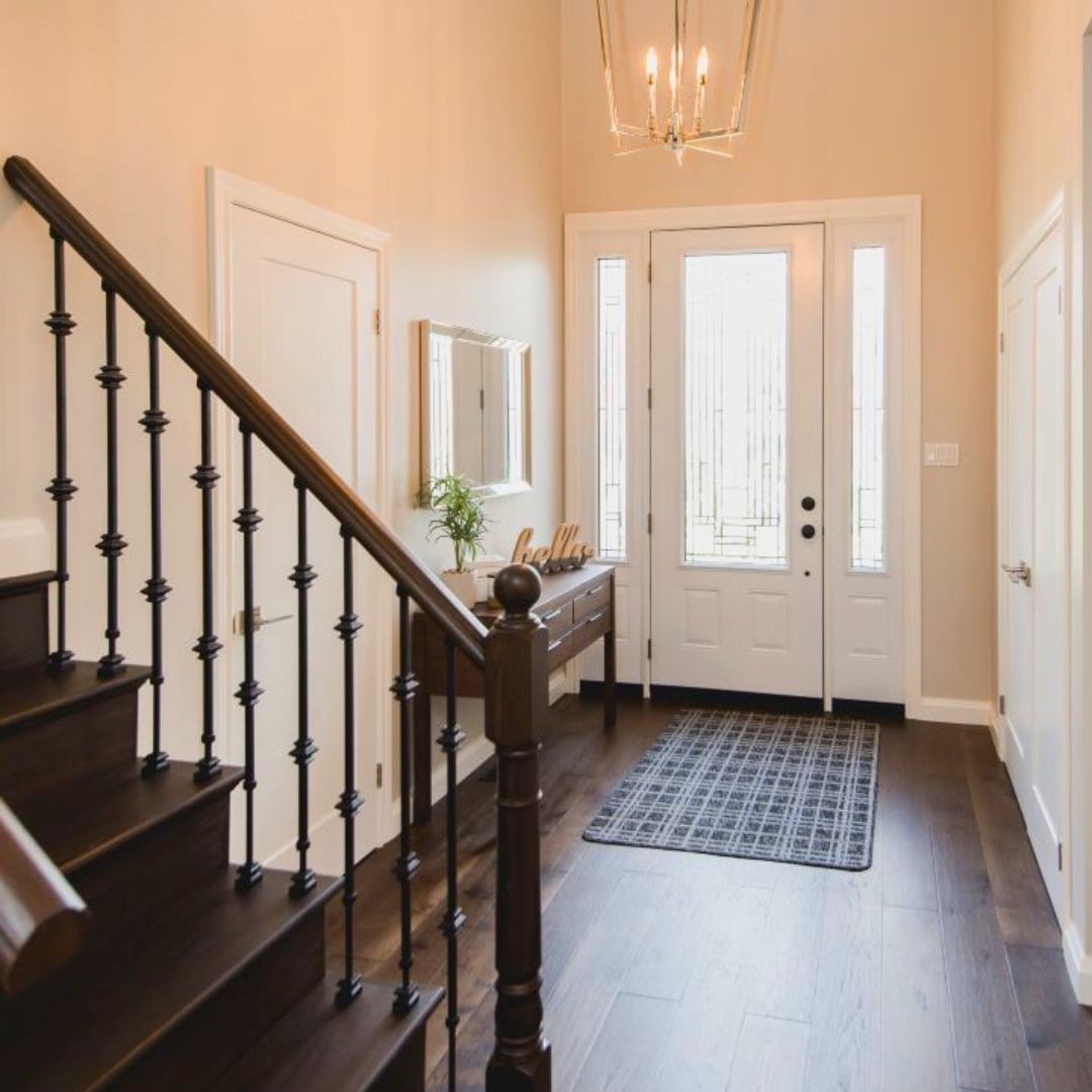 Bright entryway with white walls, dark wood stairs, and modern chandelier. Glass front door lets in natural light.