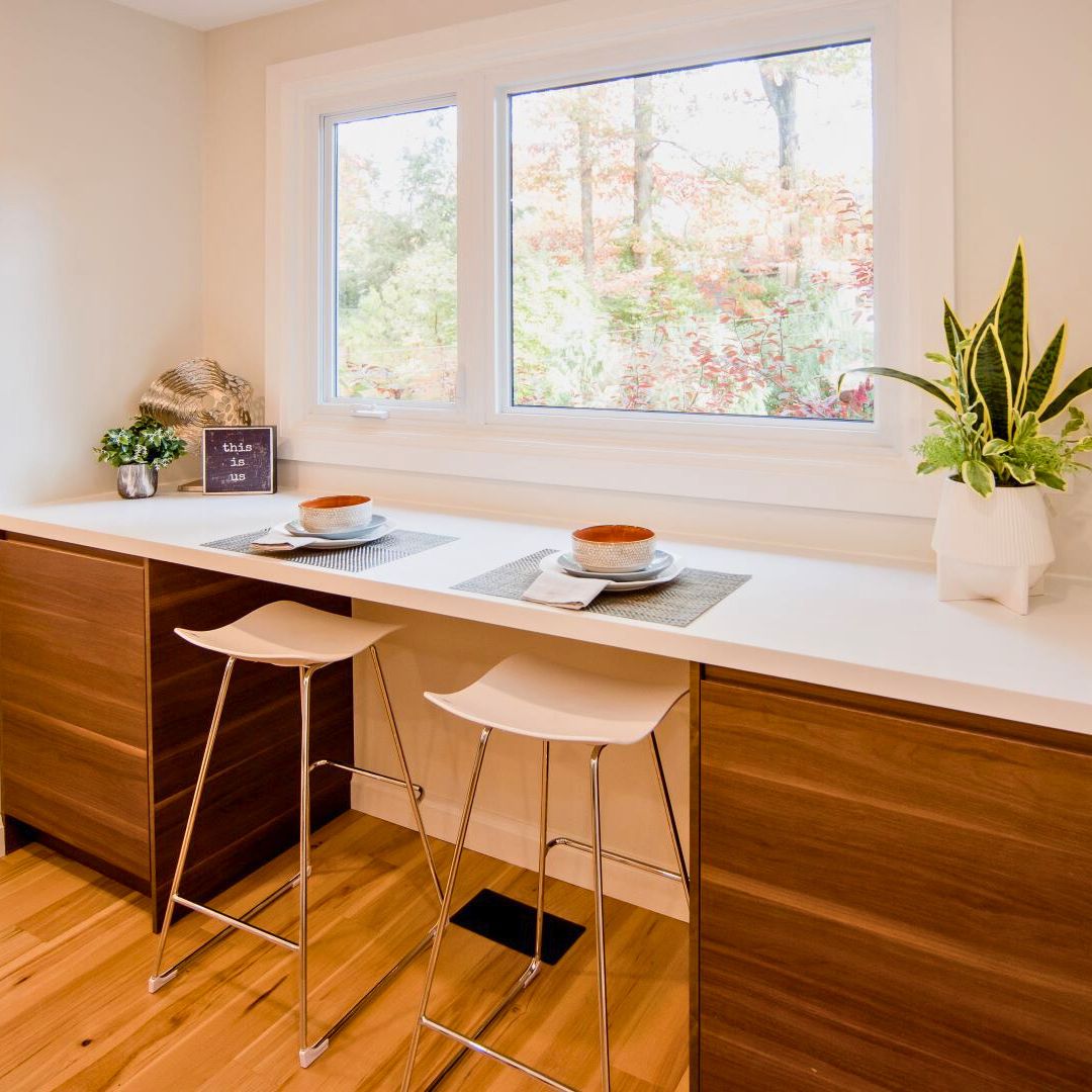 Bright kitchen nook in Hamilton home with wood cabinets, white countertop, stylish barstools, and large windows showcasing fall foliage