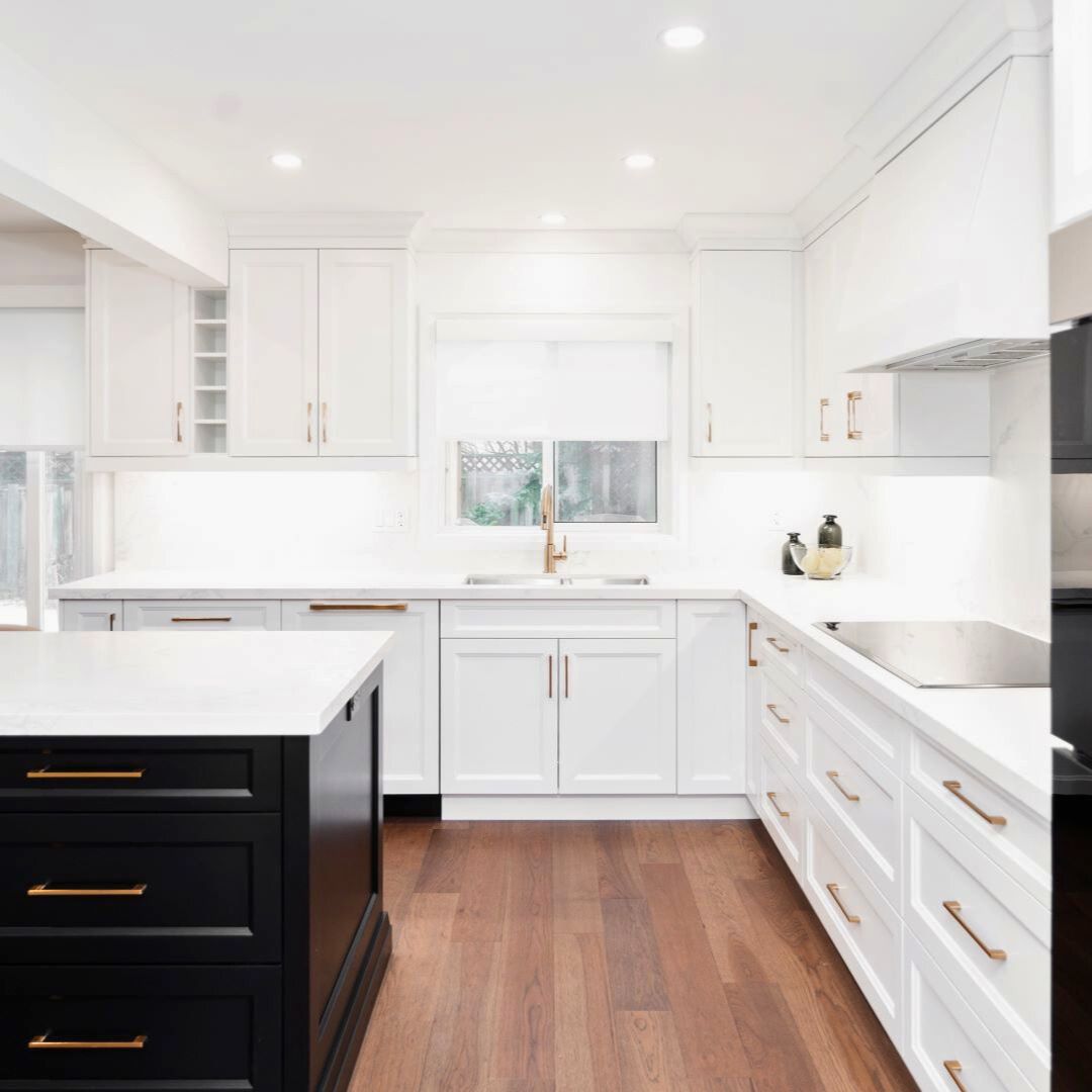 Modern white kitchen remodel showcasing a large island with contrasting black cabinetry, sleek gold hardware, and custom white cabinets. Features a bright, open design with natural light, polished countertops, and a spacious layout for a contemporary home interior upgrade.