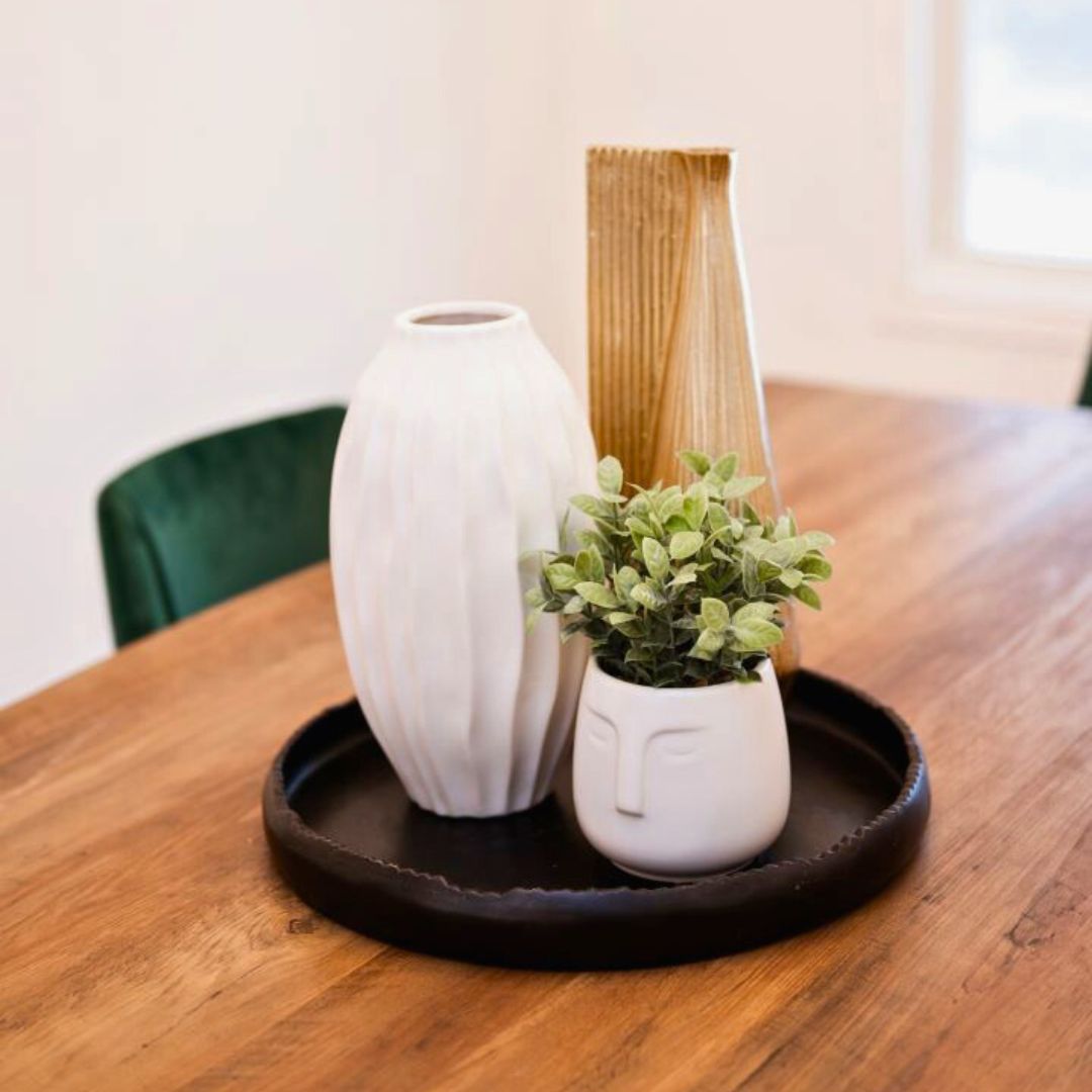 Modern dining table decor featuring a white vase, gold accent vase, and a small potted plant on a round black tray.