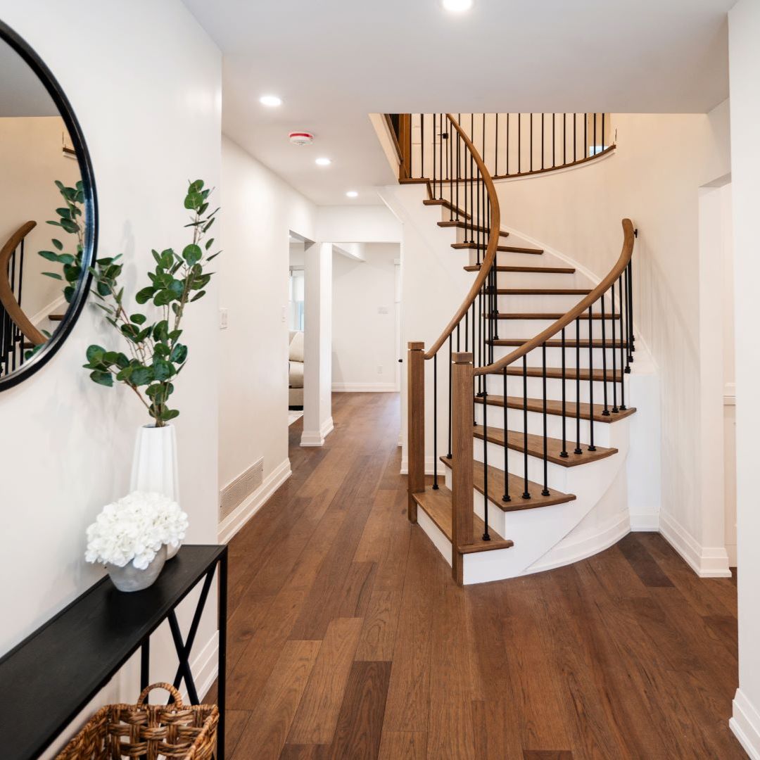 Modern hallway design featuring a beautiful spiral staircase with a wooden handrail and black iron balusters. Includes rich wood flooring, neutral walls, and stylish decor