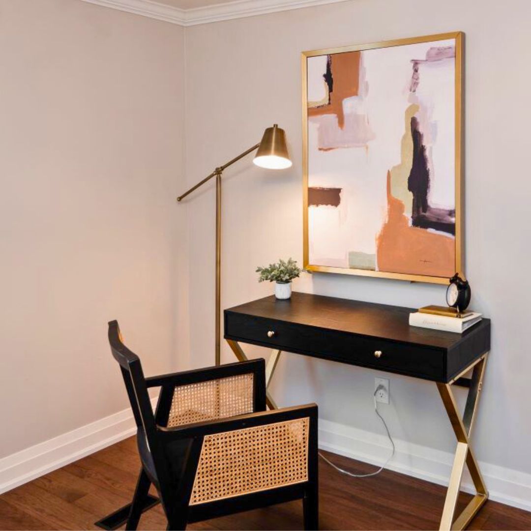 Modern home office setup featuring a black desk with gold accents, an abstract art piece, and a stylish lamp.