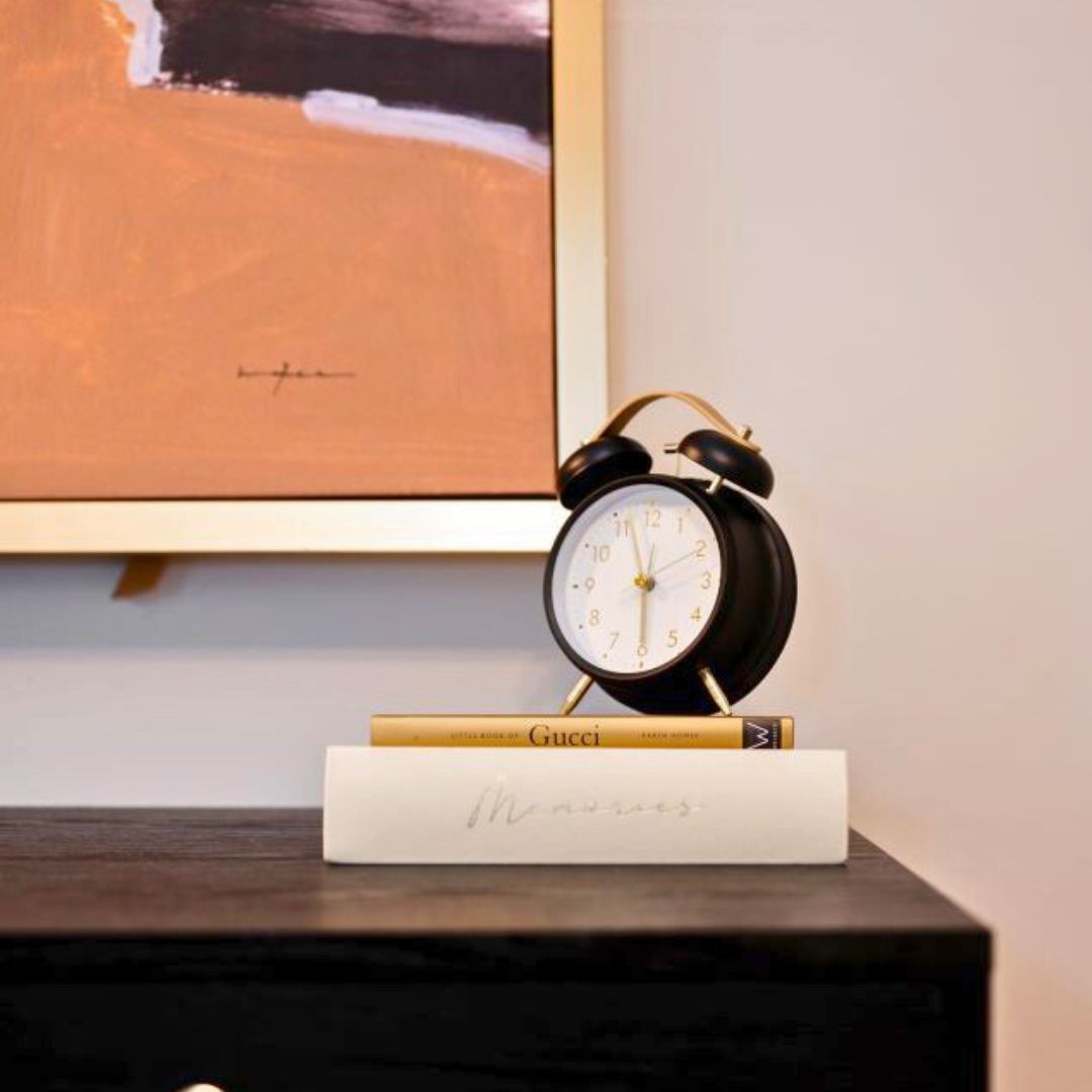 Modern office desk decor  featuring a classic black and gold clock, a decorative book, and a stylish art piece in the background.