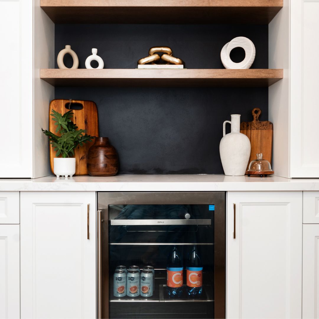 Modern kitchen nook featuring open wood shelving, minimalist decor, and a built-in wine fridge. Includes contemporary styling with contrasting dark backsplash, white cabinetry, and elegant decor accents
