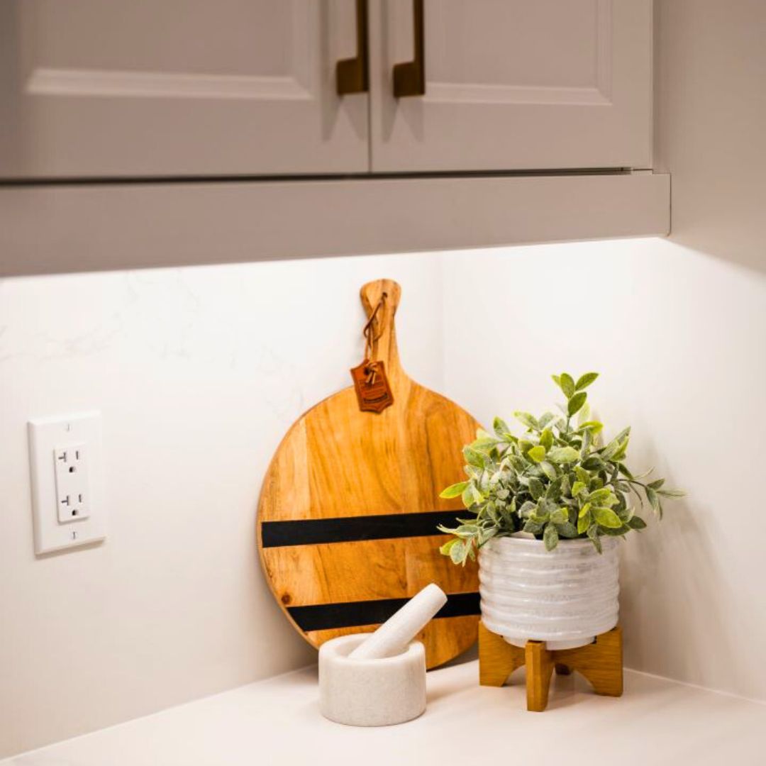 Modern kitchen decor featuring a wooden cutting board, small potted plant, and marble mortar and pestle. 