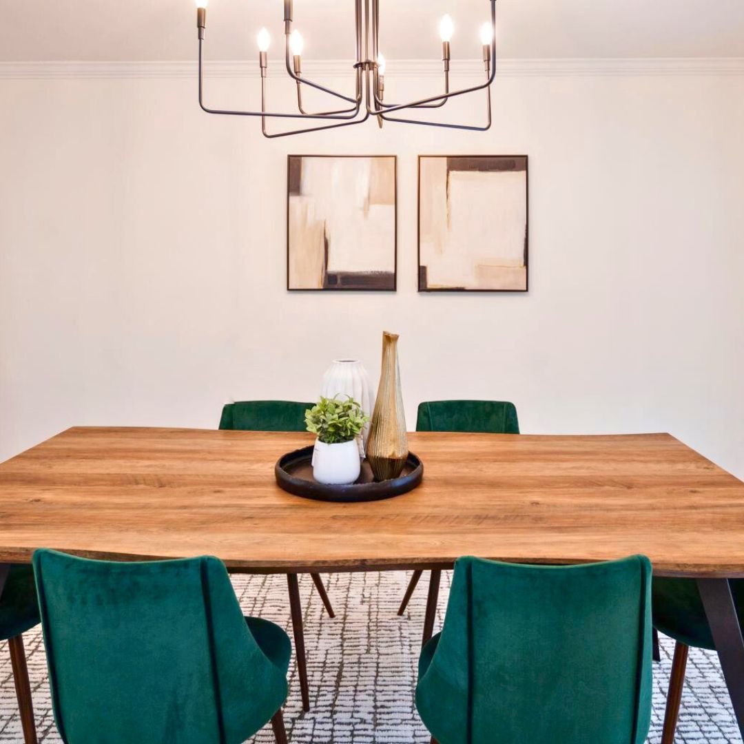 Contemporary dining room design featuring a large wooden table paired with green velvet chairs, modern abstract wall art, and a minimalist chandelier.
