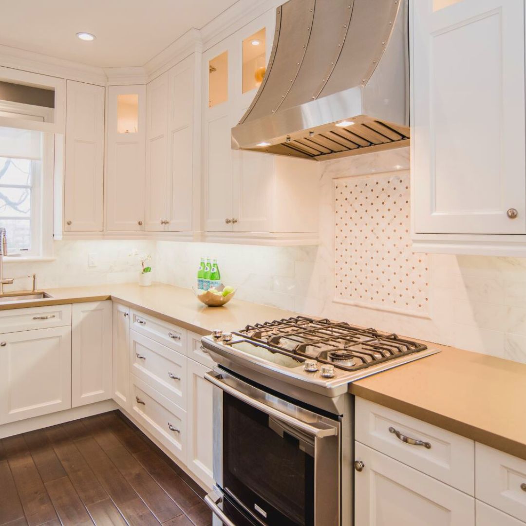 Modern kitchen featuring stainless steel range hood, gas cooktop, and tiled backsplash. White cabinets and light counters create an airy feel.