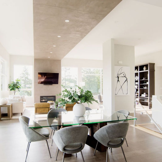 Stunning modern living room design with floor-to-ceiling windows, showcasing natural light and lush outdoor views. Features sleek white sofa, contemporary tan leather chairs, and minimalist wooden coffee table. Focal point includes wall-mounted TV above linear fireplace, perfect for entertainment. Built-in bookshelves add storage and style.