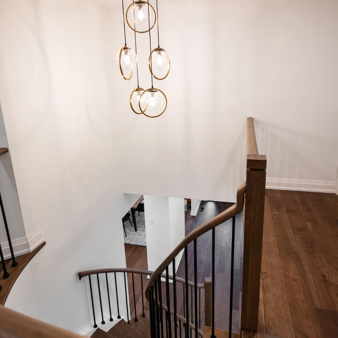 Modern staircase lighting design in Hamilton, Ontario featuring a unique glass orb chandelier with gold accent rings. The lighting fixture is paired with a curved wooden staircase and black iron balusters.