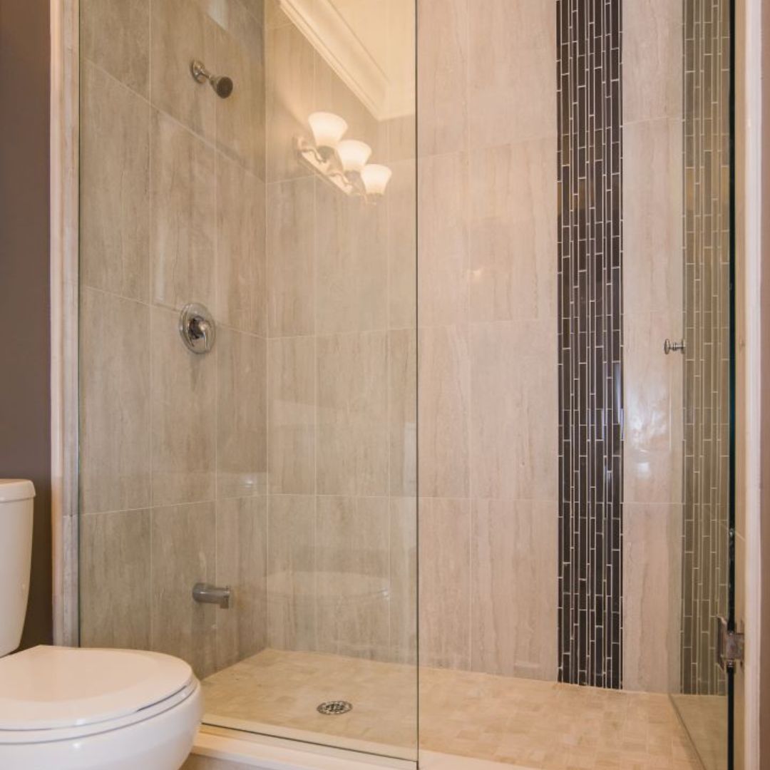 Sleek walk-in shower with glass door, beige tile walls, and a decorative vertical tile accent strip, offering a contemporary and spa-like bathroom experience.