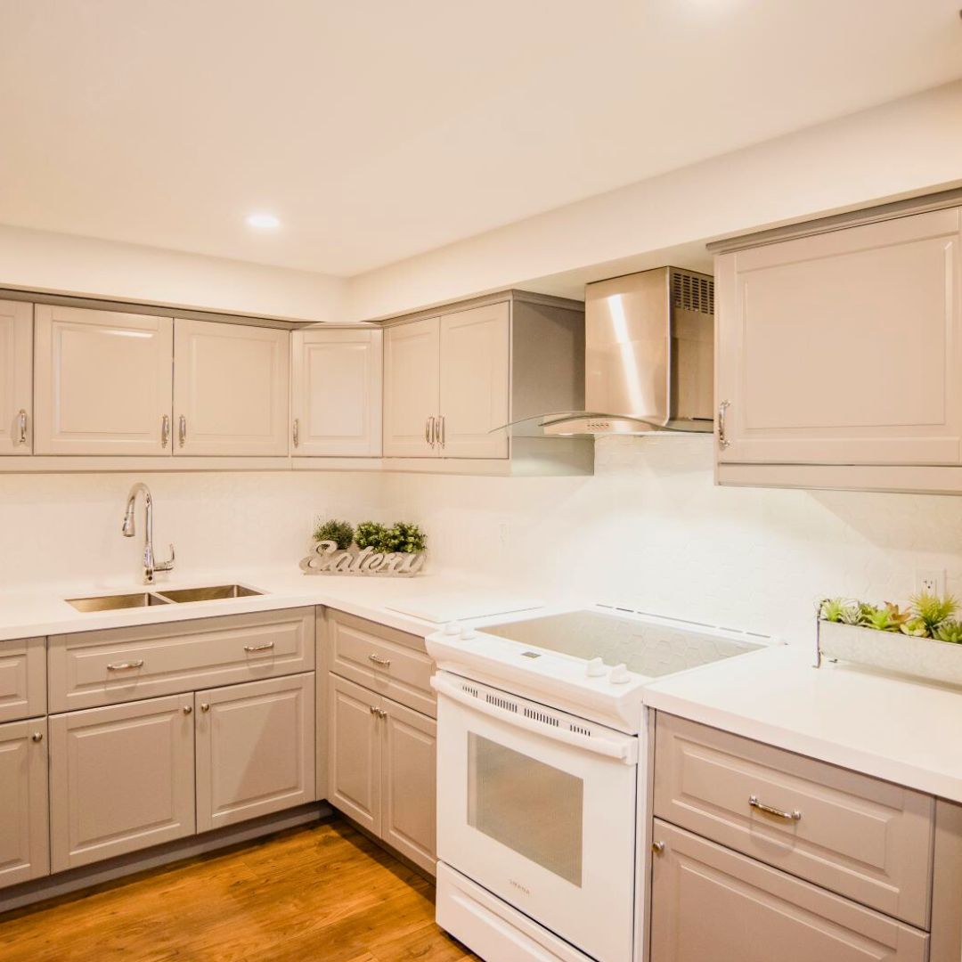 Modern kitchen with white shaker cabinets, stainless steel appliances, and wood flooring. Bright recessed lighting illuminates the space