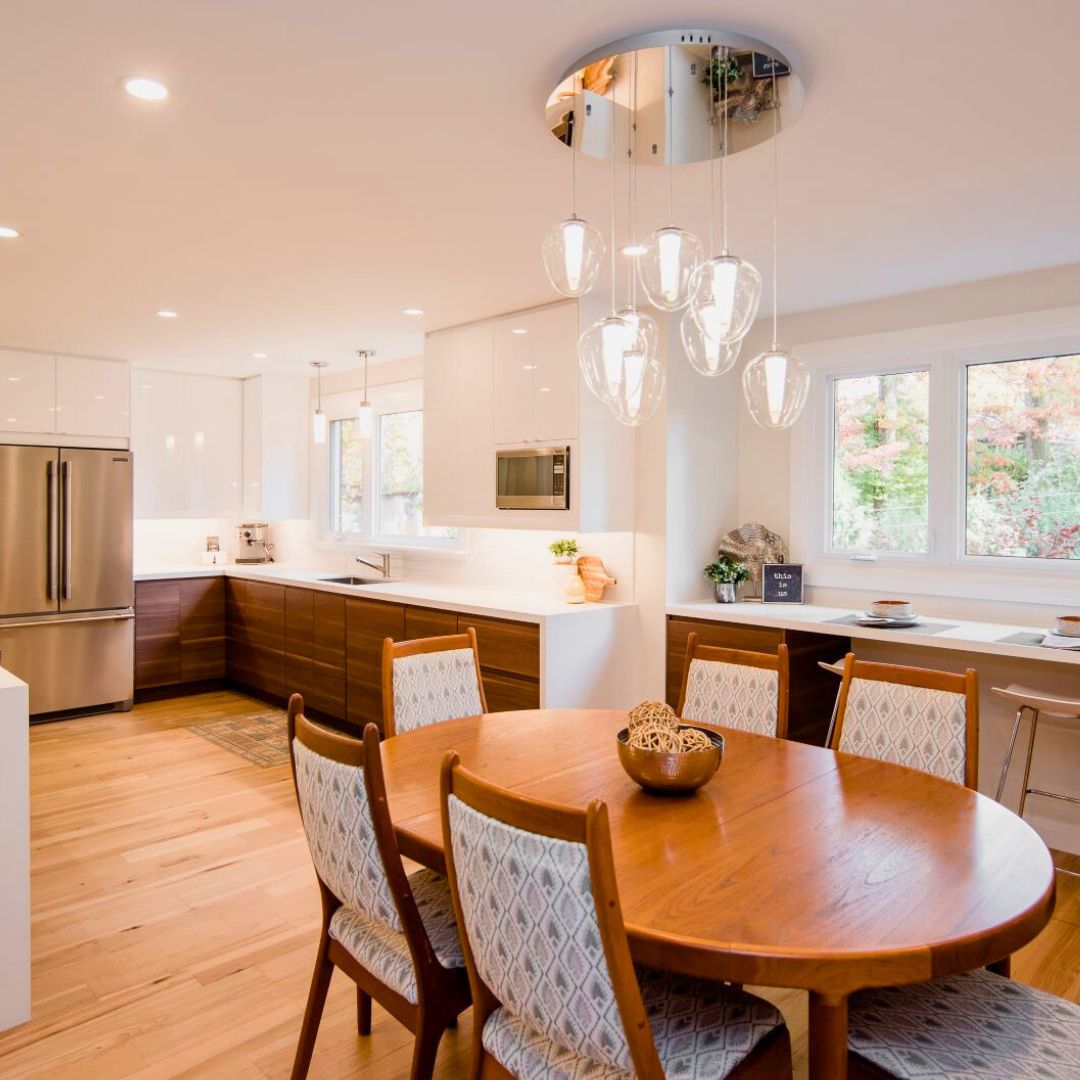 Bright open-concept kitchen and dining area with wood table, white chairs, and unique glass pendant lights hanging from circular ceiling fixture