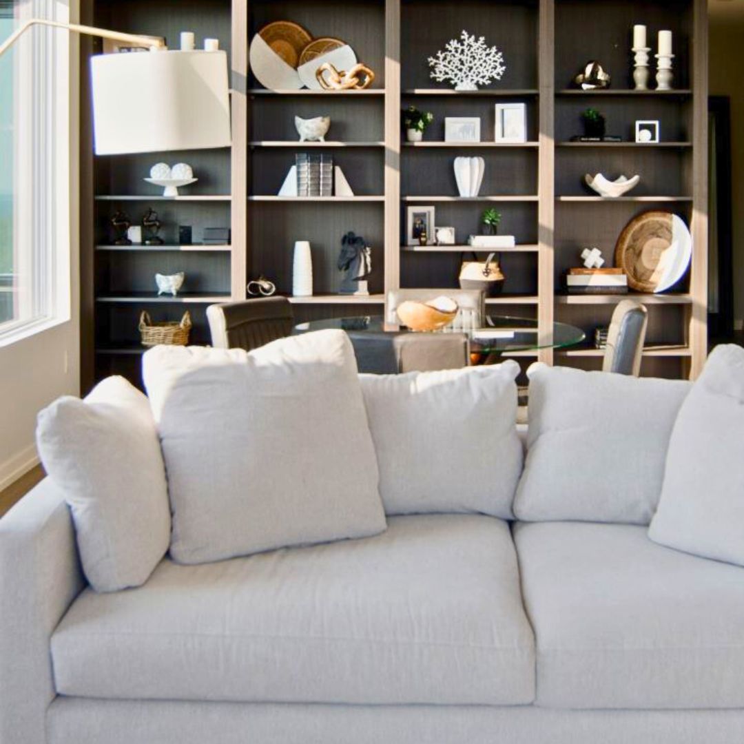 Spacious open-concept living area featuring floor-to-ceiling dark bookshelf wall. Glass dining table, leather chairs, and plush white sofa create a sophisticated, comfortable atmosphere.