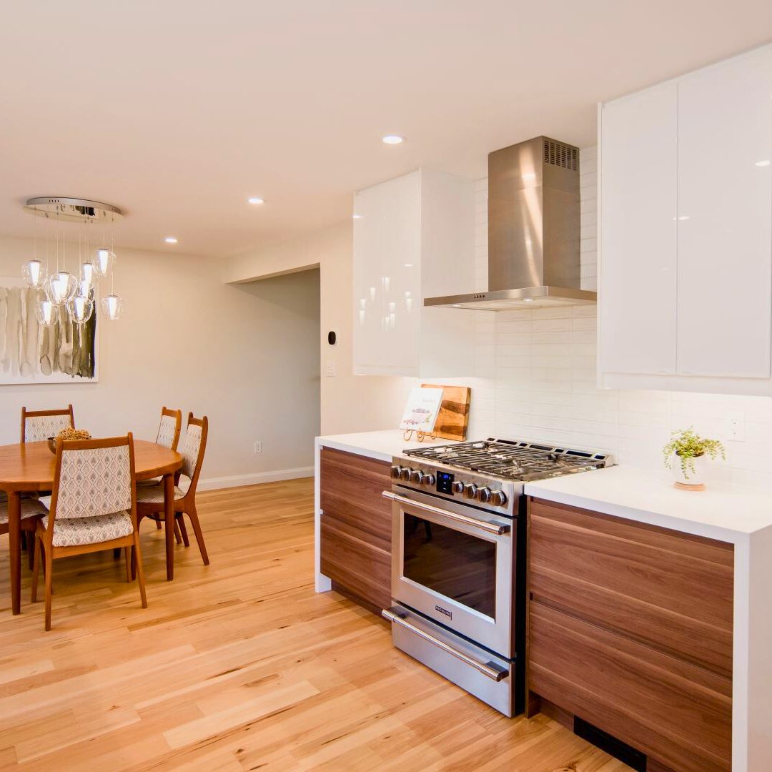 Bright open-plan kitchen and dining area boasting walnut lower cabinets, white upper cabinets, hardwood floors, stylish pendant lights over island, and mid-century modern dining set in Hamilton home redesign